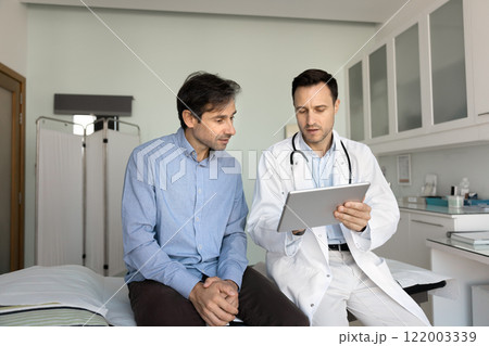 Serious doctor showing electronic checkup results to patient Serious doctor showing electronic checkup results to patient 122003339