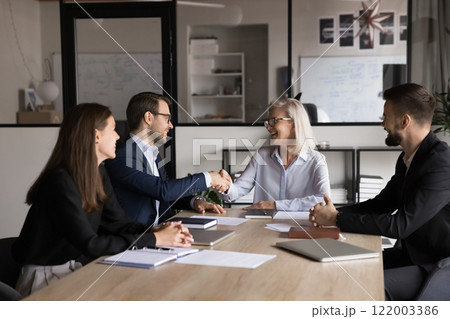 Two business partners shaking hands seated around office table Two business partners shaking hands seated around office table 122003386