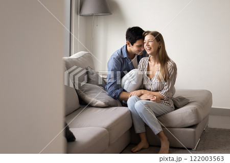 Happy young couple in love sitting close on soft couch Happy young couple in love sitting close on soft couch 122003563