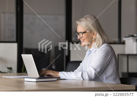 Smiling mature businesslady typing on laptop keyboard Smiling mature businesslady typing on laptop keyboard 122003577