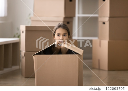 Serious pensive little girl sitting inside cardboard box 122003705