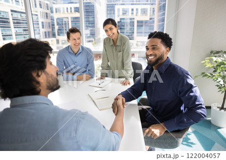 Happy young African businessman shaking hand with male Indian partner Happy young African businessman shaking hand with male Indian partner 122004057