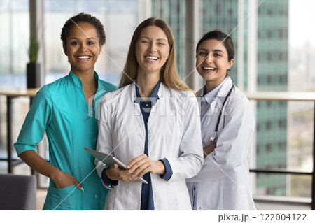 Group of three female doctors stand together, smiling at camera 122004122