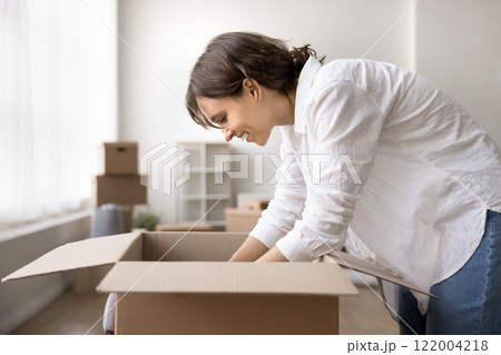 Young woman unpacking her belongings stacked in boxes 122004218