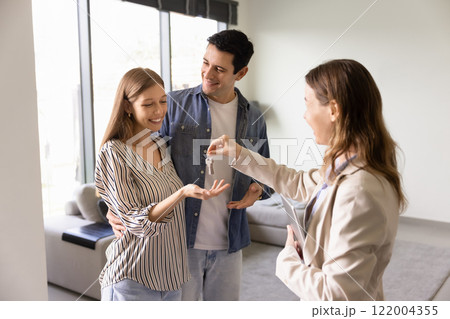 Real estate agent woman giving key to young couple 122004355