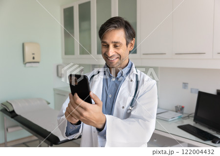 Positive middle aged Latin doctor man using application on phone Positive middle aged Latin doctor man using application on phone 122004432