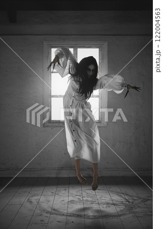 Woman with dark hair and claws, in white dress levitating in the air above the floor with ash. 122004563