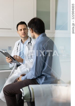 Focused concerned doctor examining male patient, working in clinic Focused concerned doctor examining male patient, working in clinic 122004803