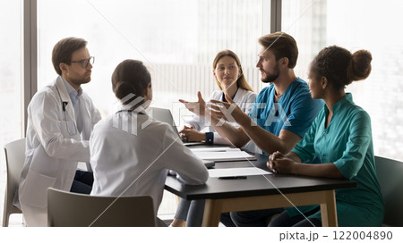 Young doctor make speech during briefing with diverse clinic workmates Young doctor make speech during briefing with diverse clinic workmates 122004890