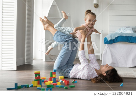 Laughing mum play airplane with excited little daughter on floor Laughing mum play airplane with excited little daughter on floor 122004921