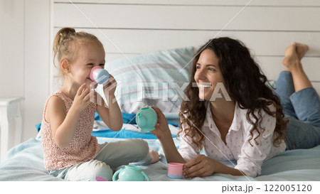 Young mom little girl play toy tea set on bed Young mom little girl play toy tea set on bed 122005120
