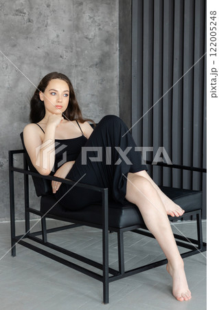 Young woman relaxing on a modern black armchair in a minimalist interior Young woman relaxing on a modern black armchair in a minimalist interior 122005248
