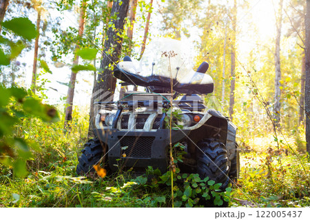 Quad bike or ATV in tall grass in sunny autumn forest. All Terrain Vehicle of hunter or forester outside. front view of Quadbike Quad bike or ATV in tall grass in sunny autumn forest. All Terrain Vehicle of hunter or forester outside. front view of Quadbike 122005437