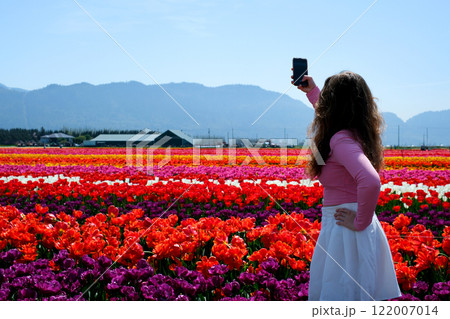 Portrait of a happy woman with hair flying in the wind against the backdrop of mountains and sea. Holding a bouquet of tulips Portrait of a happy woman with hair flying in the wind against the backdrop of mountains and sea. Holding a bouquet of tulips 122007014