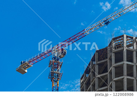 Construction crane, multi-story building under construction in process of erecting load-bearing elements of frame made of monolithic reinforced concrete on sky background. House building industry Construction crane, multi-story building under construction in process of erecting load-bearing elements of frame made of monolithic reinforced concrete on sky background. House building industry 122008986