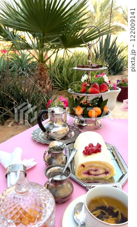 Creamy cake roll placed next to cup on wooden table, ornate silver tray adding rustic elegance. Cup and cake together enhance outdoor dessert ambiance. Wooden display concept. 122009141