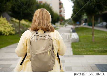 Rear view of young female tourist backpacker with headphones walking on the street. Closeup of woman resting outdoors. Urban lifestyle concept Rear view of young female tourist backpacker with headphones walking on the street. Closeup of woman resting outdoors. Urban lifestyle concept 122010231