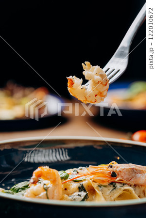 Fork lifting a perfectly cooked shrimp from a creamy pasta dish, a delightful seafood indulgence Fork lifting a perfectly cooked shrimp from a creamy pasta dish, a delightful seafood indulgence 122010672