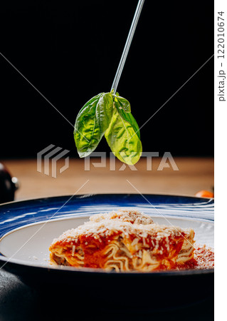 Fresh basil leaves hovering over a delicious lasagna dish, showcasing vibrant Italian flavors Fresh basil leaves hovering over a delicious lasagna dish, showcasing vibrant Italian flavors 122010674