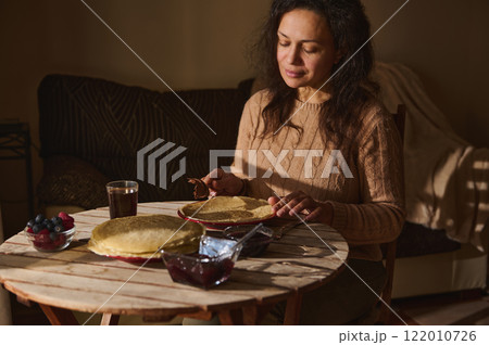 Woman enjoying pancakes with spread and fruit at a cozy kitchen table 122010726