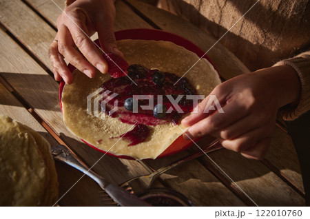 Hands Preparing a Crepe with Jelly and Fresh Berries on Wooden Table 122010760
