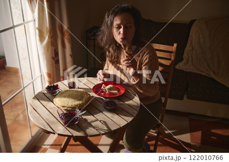 Woman enjoying a warm breakfast at a sunlit table indoors Woman enjoying a warm breakfast at a sunlit table indoors 122010766