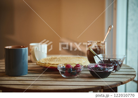 Rustic breakfast setup with crepes, berries, and spreads on a wooden table 122010770