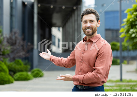 Successful man invites to work in a new team. Businessman looks at the camera and holds hands to the side in a gesture of greeting and invitation. Successful man invites to work in a new team. Businessman looks at the camera and holds hands to the side in a gesture of greeting and invitation. 122011285
