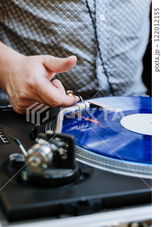 DJ spinning blue vinyl record on turntable, creating retro music vibes at an event DJ spinning blue vinyl record on turntable, creating retro music vibes at an event 122012155