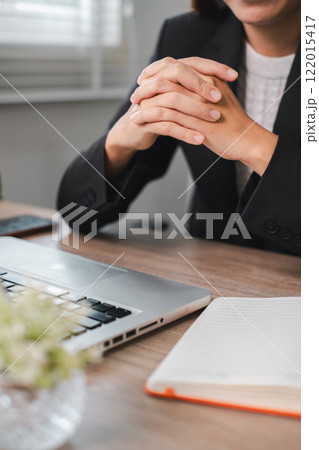 A business professional in a suit sits at a desk with a laptop and notebook, ready for work in a modern office environment. A business professional in a suit sits at a desk with a laptop and notebook, ready for work in a modern office environment. 122015417