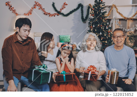 Portrait of Asian family exchanging presents during christmas at home. Attractive happy people holding gift box, celebrate holiday thanksgiving, xmas eve tradition in living room in house together. 122015852