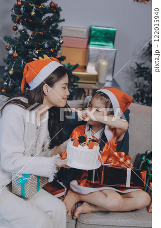 Merry Christmas and Happy Holidays. Cheerful mom and her cute daughter girl exchanging gifts. Parent and little child having fun near tree indoors. 122015940