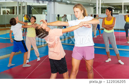 Kids in pair exercising self-defense movements during group class with female coach 122016205