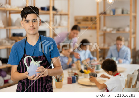 Boy in an apron holds a ceramic product Boy in an apron holds a ceramic product 122016293