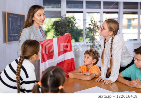School teacher tells students about Denmark and holds a Denmark flag in hands. 122016419