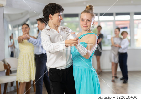 Positive teen boy and girl are dancing classic version of waltz in couple during lesson at studio Positive teen boy and girl are dancing classic version of waltz in couple during lesson at studio 122016430