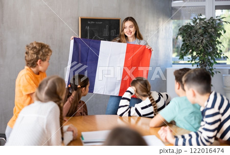 Joyful female teacher discussing with preteens students state flag of France in auditory of middle school 122016474