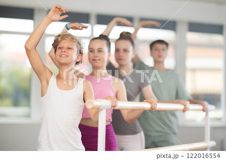 Group of teenagers stand in third position near ballet barre during group training in dance studio 122016554
