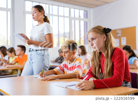 Boys an girls sitting at lesson in classroom, teacher standing Boys an girls sitting at lesson in classroom, teacher standing 122016599
