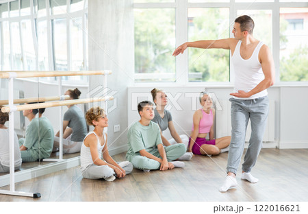 Sportive young male trainer demonstrating professional poses to teenage boys and girls 122016621