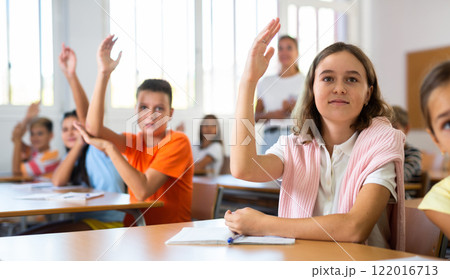 Diligent tween schoolgirl raising hand during lesson in classroom Diligent tween schoolgirl raising hand during lesson in classroom 122016713