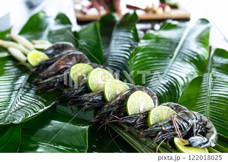 Vibrantly prepared tiger shrimp are elegantly displayed on glossy banana leaves, their natural colors highlighted by fresh lime slices, capturing the essence of Asian cuisine and creativity. Vibrantly prepared tiger shrimp are elegantly displayed on glossy banana leaves, their natural colors highlighted by fresh lime slices, capturing the essence of Asian cuisine and creativity. 122018025