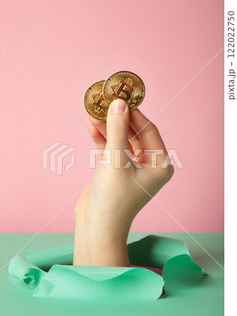 Female hand with coin of bitcoin punching through the paper Female hand with coin of bitcoin punching through the paper 122022750