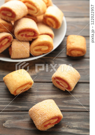 Homemade cookies, mini rolls with apricot jam in plate on brown wooden background. Vertical photo. 122022957