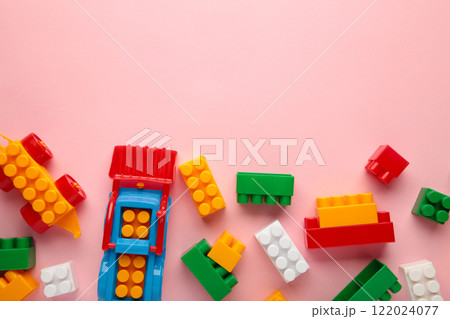 Multicolored blocks of the children's constructor lie on a pink background. Multicolored blocks of the children's constructor lie on a pink background. 122024077