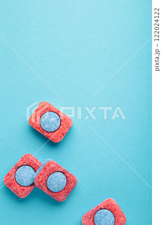 Red and blue tablets for dishwashing machine. Detergents for home hygiene. Dishwasher capsules on blue background. 122024122