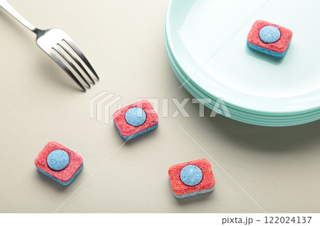 Dishwasher detergent tablet with fork and dishes on grey background. 122024137