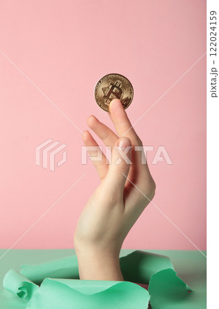 Female hand with coin of bitcoin punching through the pink paper 122024159