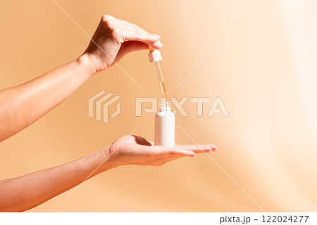 Female hands hold white serum bottle. Beauty routine. 122024277