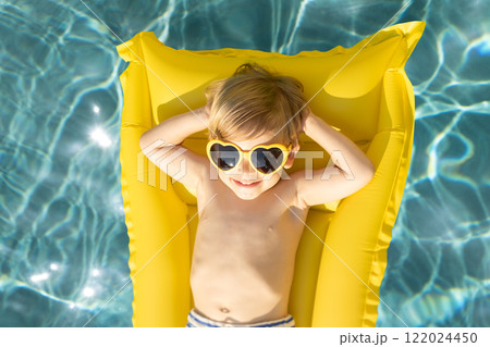 Funny kid lying on yellow mattress in swimming pool 122024450